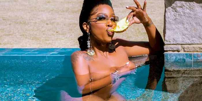 Cropped photo of a naked black woman eating fruit while submerged in a pool