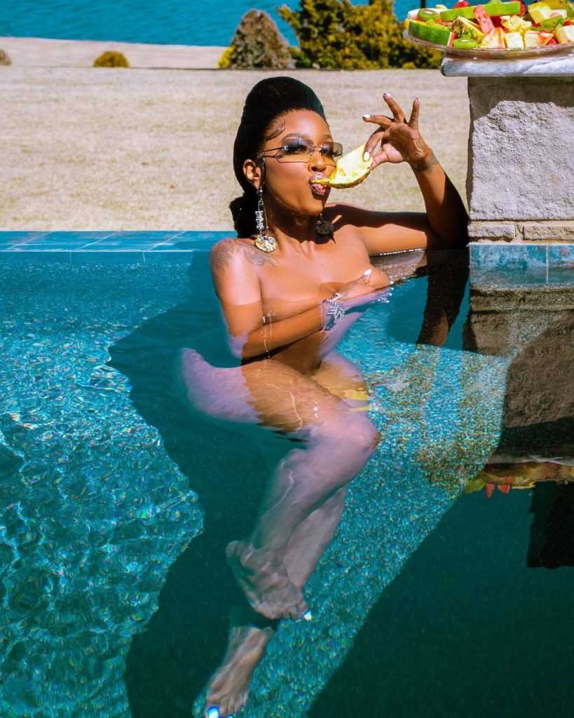 Black woman nude in a pool and eating a slice of Pineapple