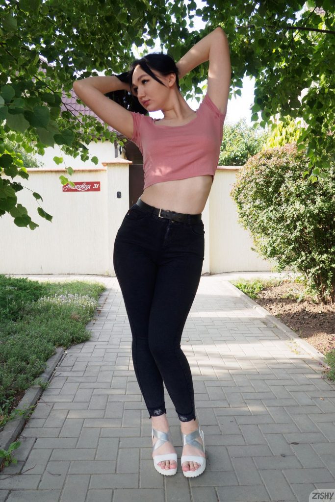 Frontal view of girl posing outdoors with her arms raised above her head