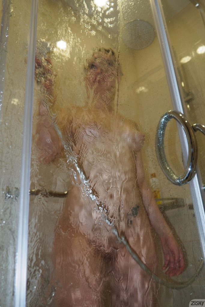 Looking up at nude girl standing behind shower glass showing her front