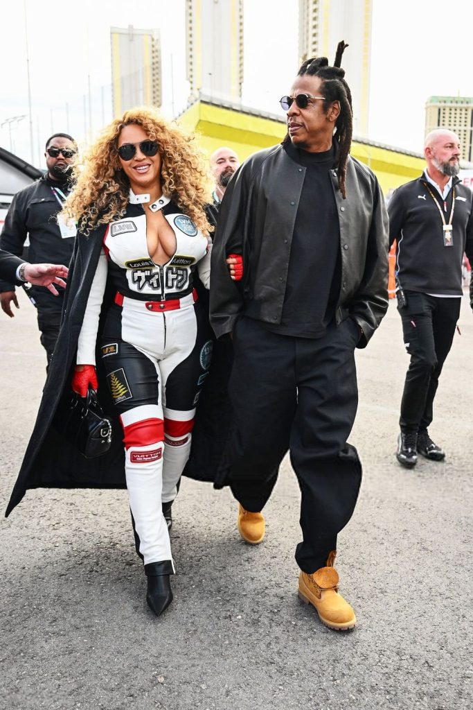 Full body frontal of Beyonce wearing a racing outfit while walking next to Jay-Z