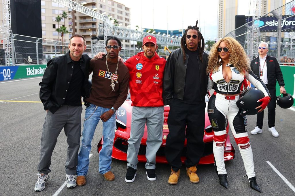 Horizontal full body frontal view of Beyonce, Jay-Z, Lewis Hamilton and others posing in front of a racing car