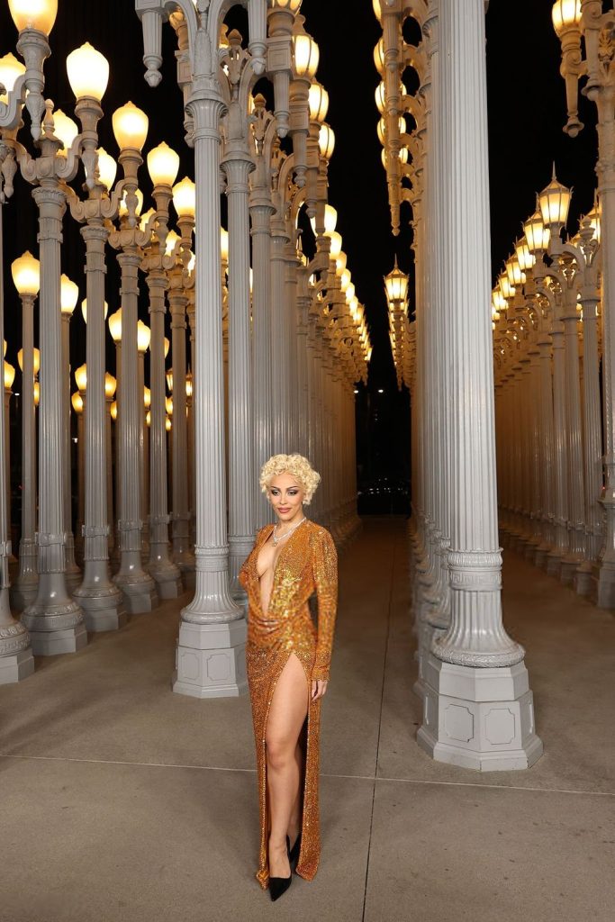 Very far away view of Doja Cat posing with one leg to the front by tall street lights