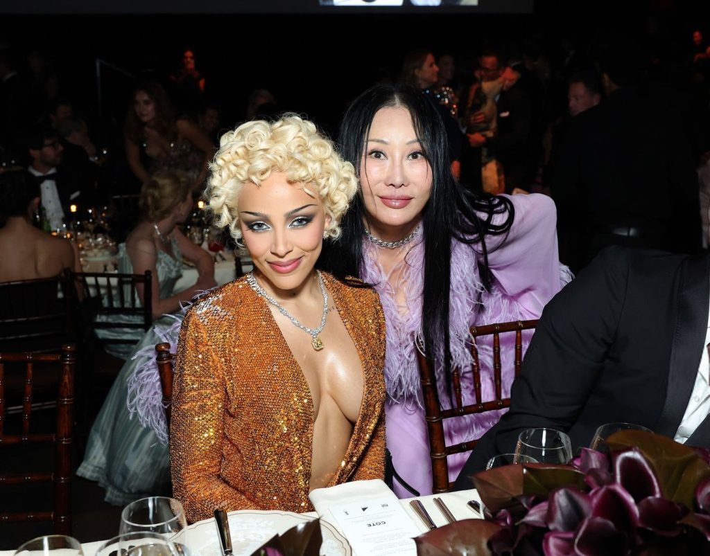 Doja Cat sitting at a table with an Asian woman leaning in