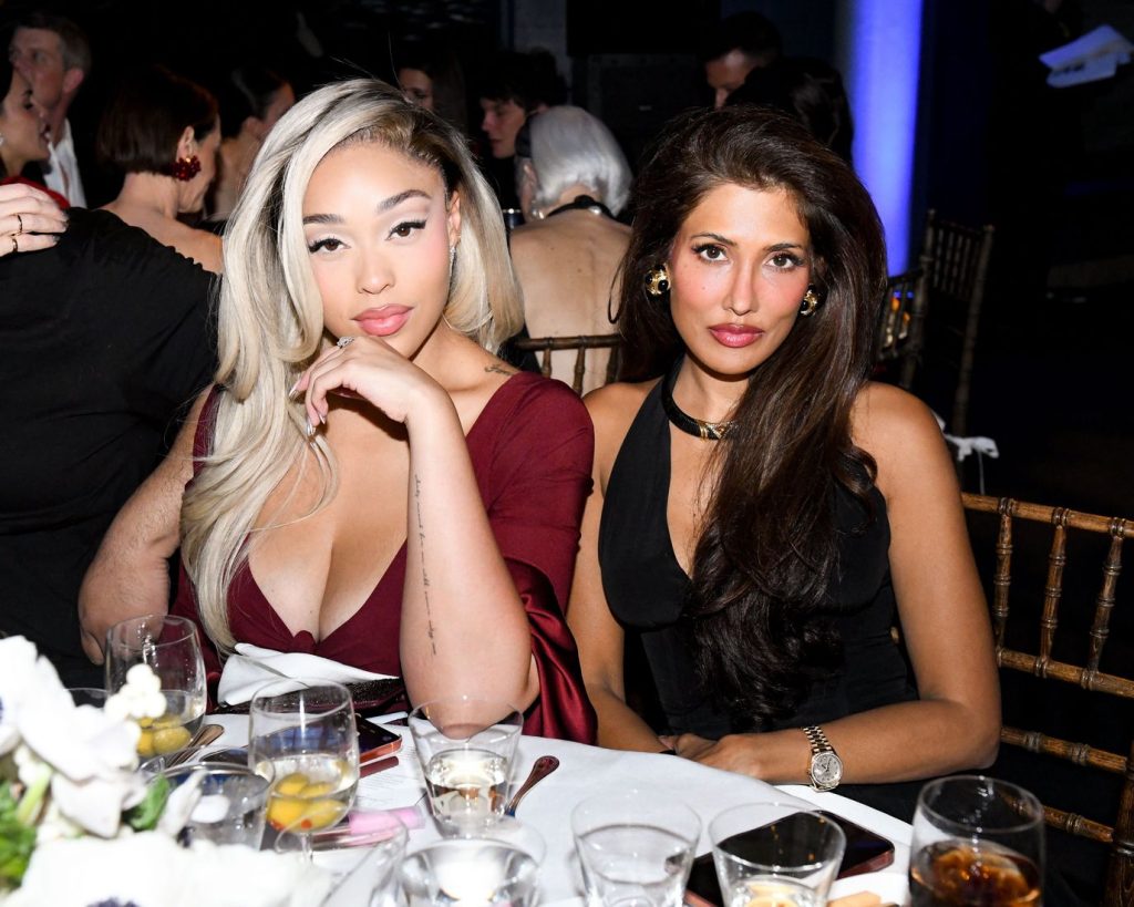 Frontal view of Jordyn Woods sitting at a dinner table with another woman