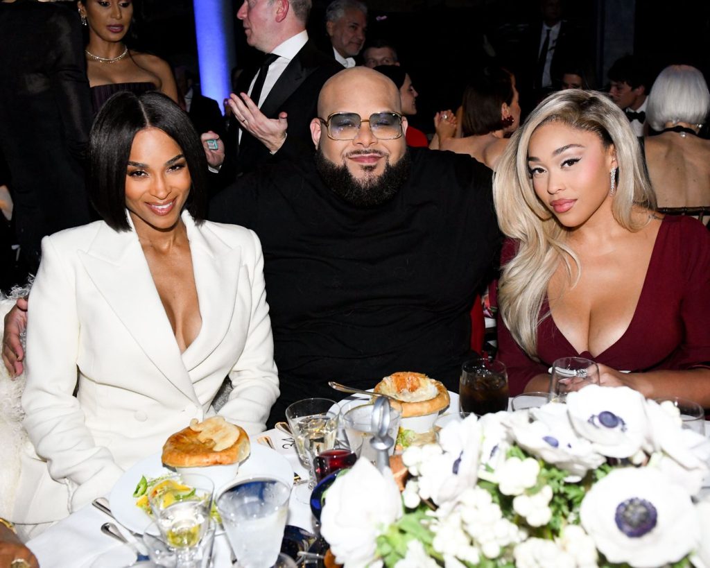 Frontal view of Jordyn Woods sitting at a dinner table next to another woman and a man sitting between them