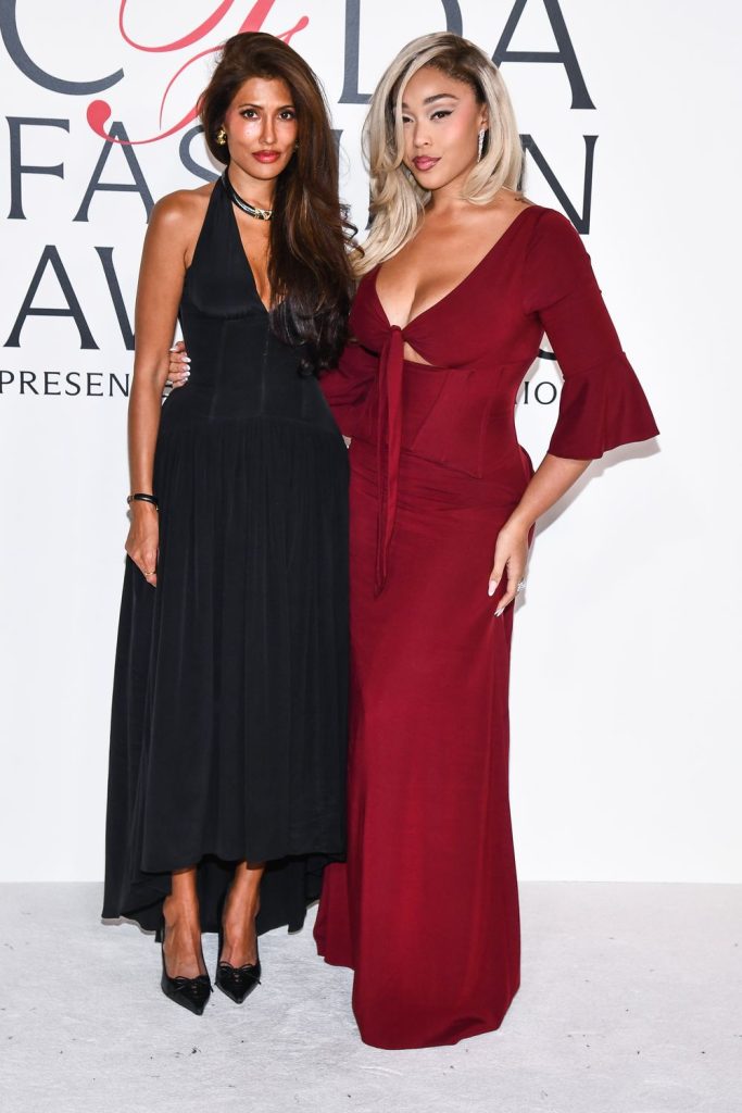 Full body view of Jordyn Woods posing at an event with another woman who smiles