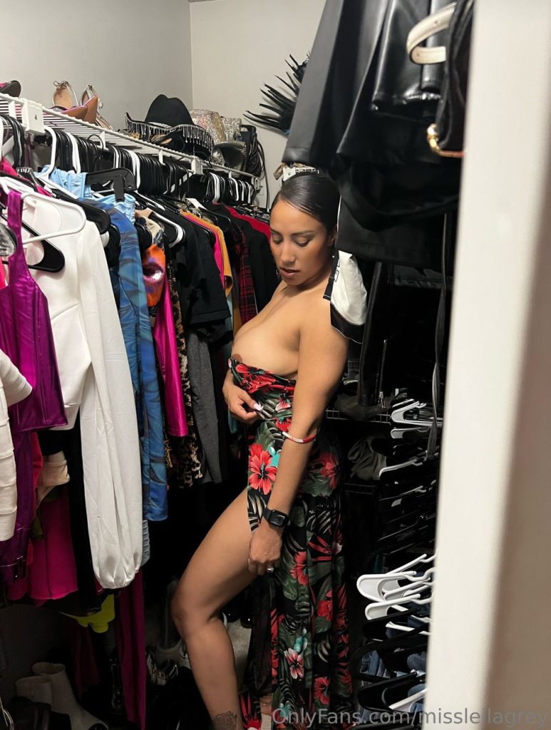 Full body view of Leila Grey standing on her side inside a closet and pulling down her dress to reveal half of her breasts
