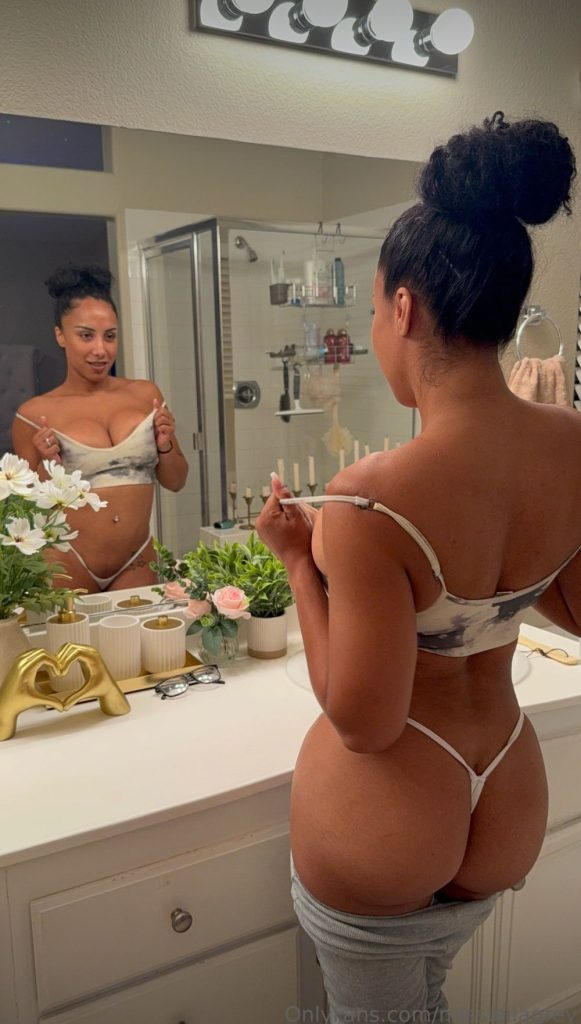 Leila Grey wearing string underwear and a bra while looking at herself in a bathroom mirror