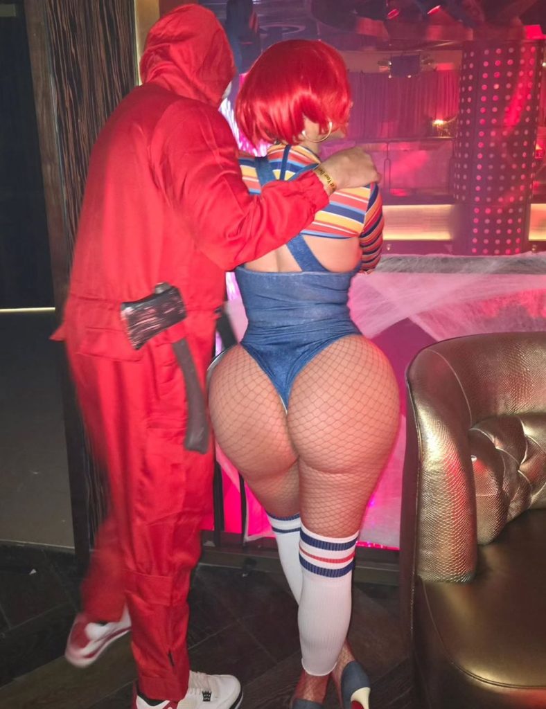 Full body view from behind of a man putting his arm around the shoulder of a curvy woman wearing a Chucky costume