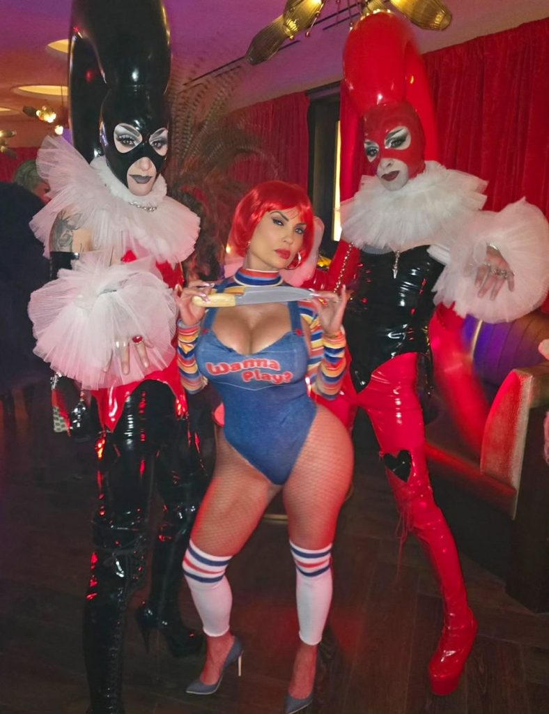 Full body front view of woman in a Chucky costume posing between two tall people dressed as Jokers