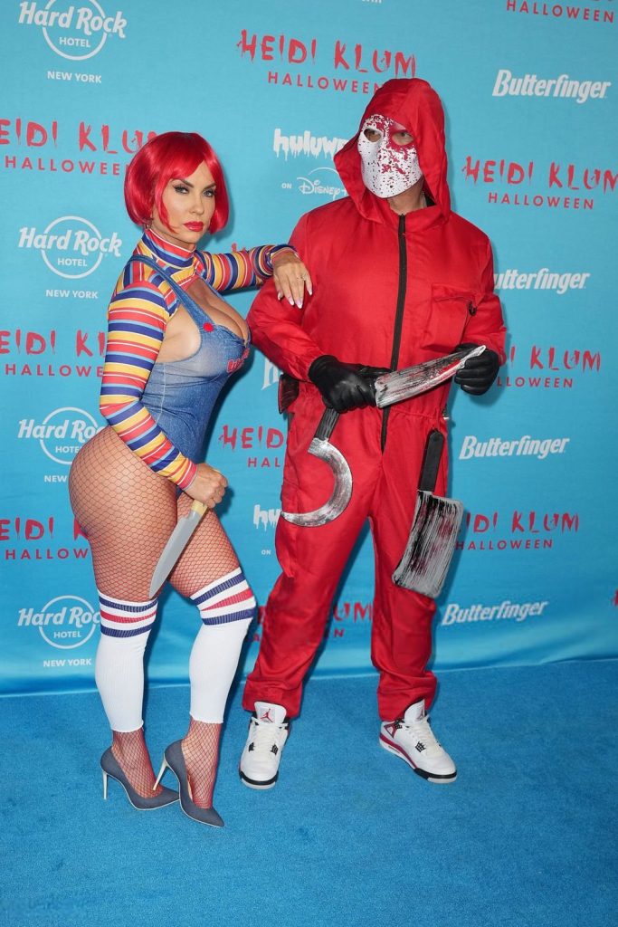 Full body view of curvy woman turned to the side in a Chucky costume and next to a man wearing a scary Halloween costume