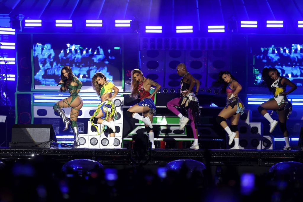 Far away side view of Anitta and her dancers raising a leg on stage