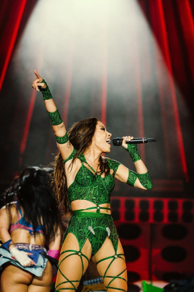 Frontal view of Anitta with one arm raised as she sings into a microphone