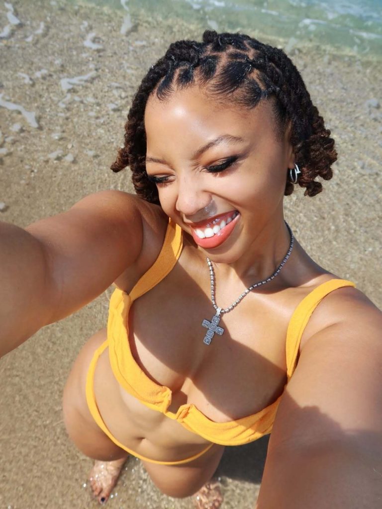 Chloe Bailey holding a camera above her head for a selfie at the beach