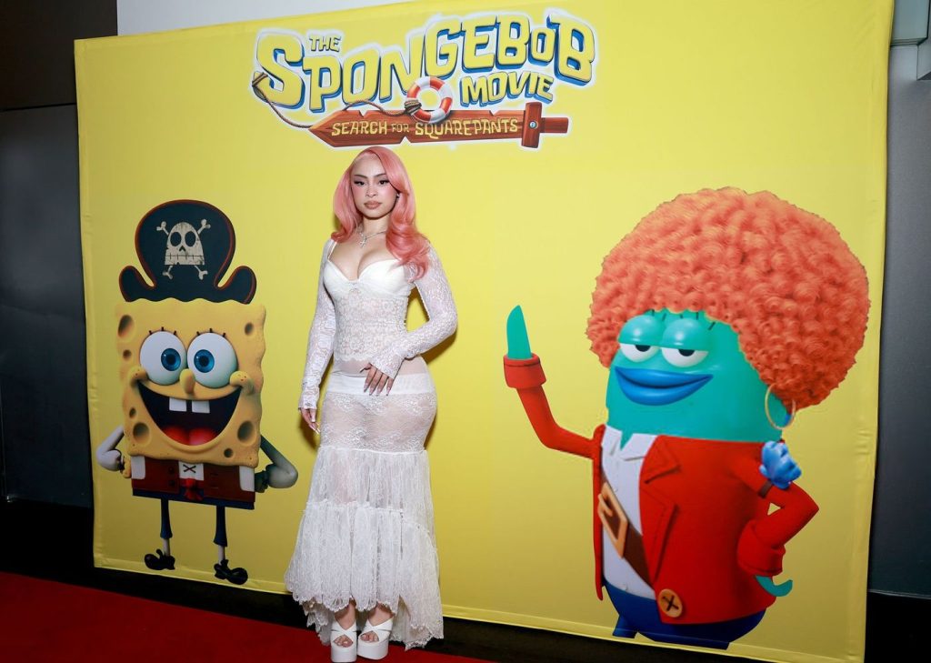 Far away frontal of Ice Spice posing between two SpongeBob characters on a red carpet