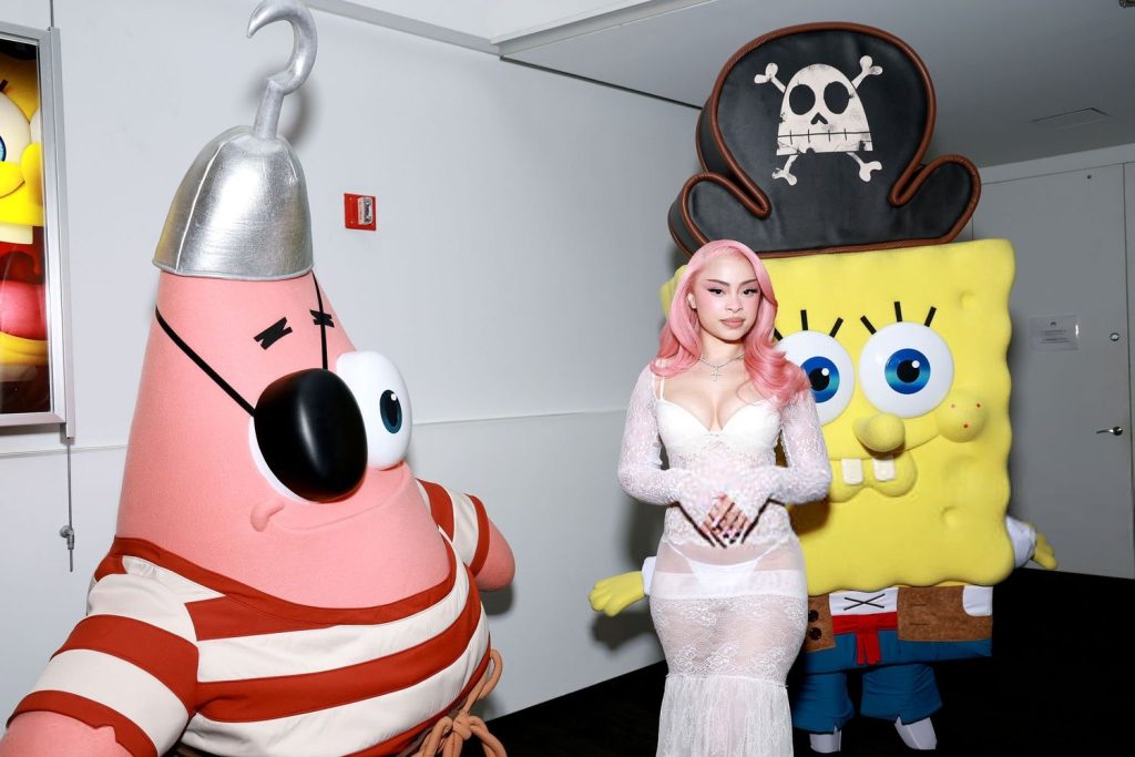 Frontal of Ice Spice posing between two SpongeBob characters on a red carpet