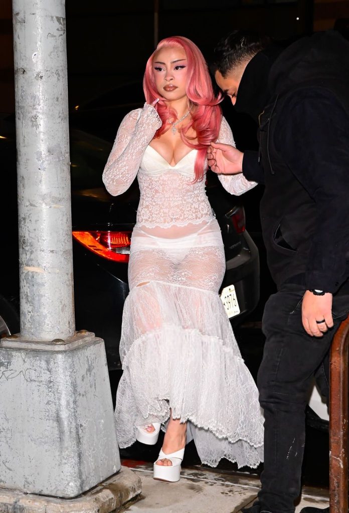 Full body frontal of Ice Spice getting help up a curb while wearing a semi-sheer dress