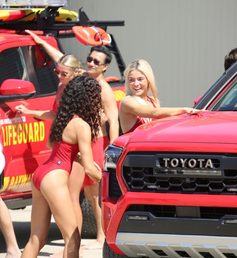 Two women lifeguards in swimsuits washing cars at beach