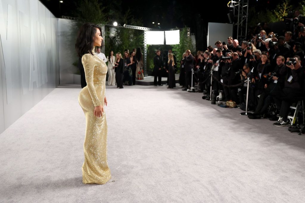 Far away view of Kim Kardashian standing on red carpet with photographers taking photos.