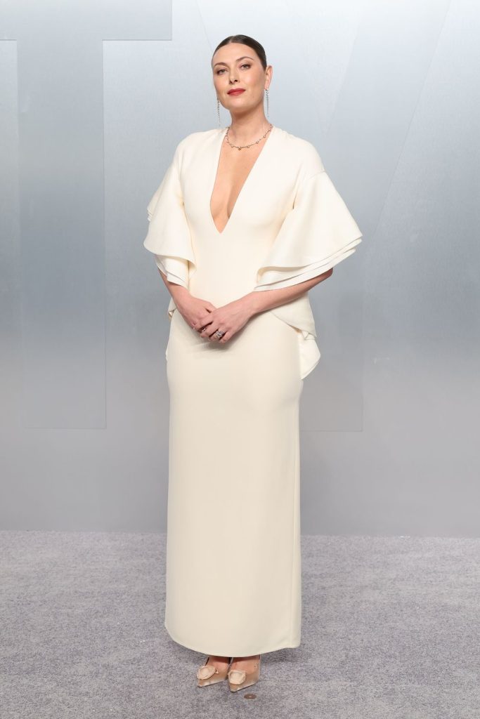 Elegant woman standing and clasping her hands in white dress.