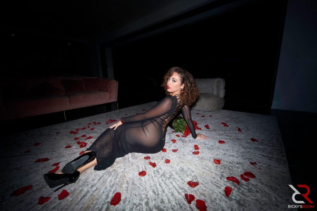 Profile view of ebony woman in sheer dress sitting on a bed covered with rose petals