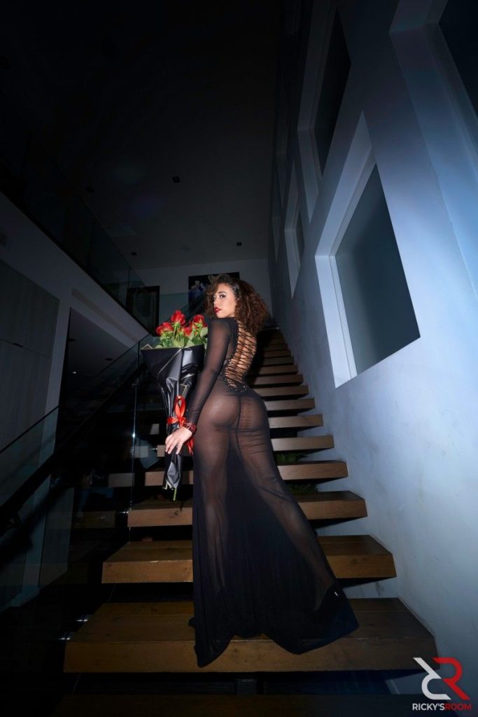 Ebony woman in sheer dress showing her backside and holding up roses on stairs