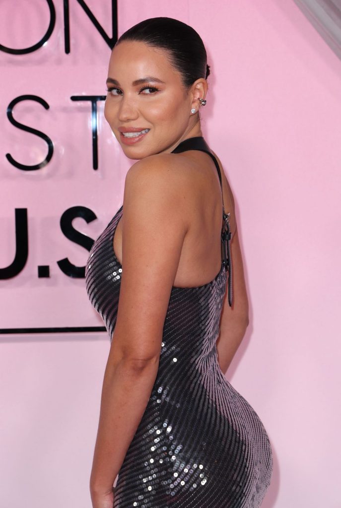 Close up side view of black woman in a glittery dress in front of a sign and pink wall.