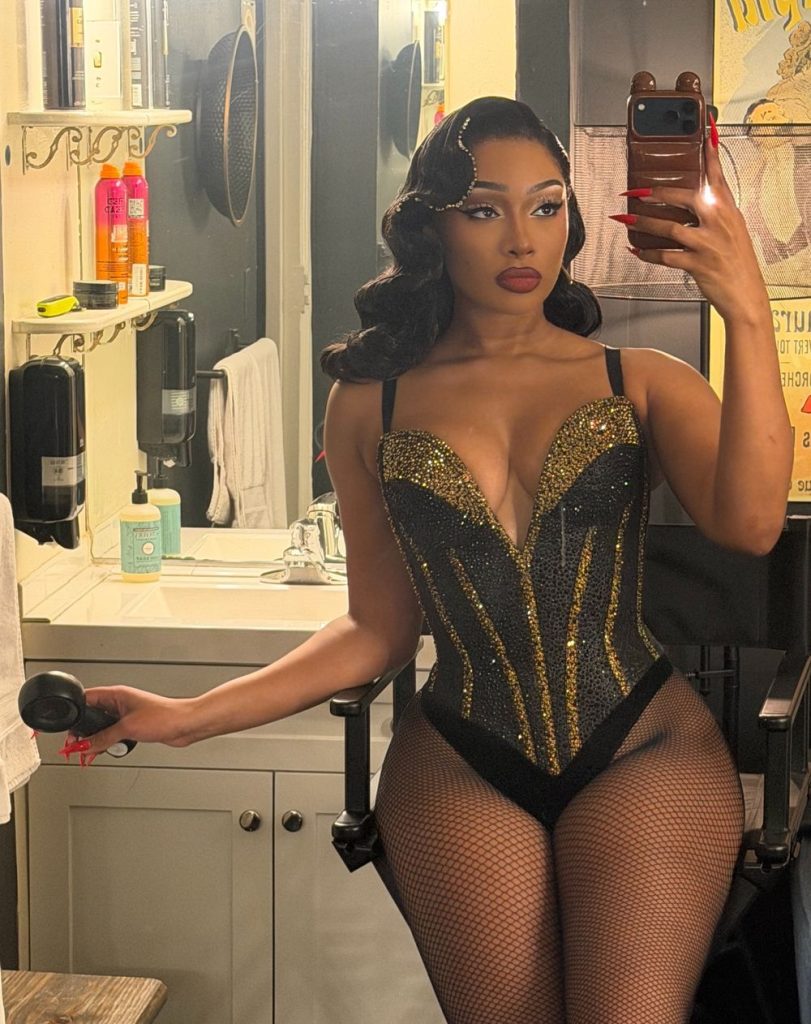 Megan Thee Stallion wearing a corset taking a selfie in a dressing room with a mirror in the background.