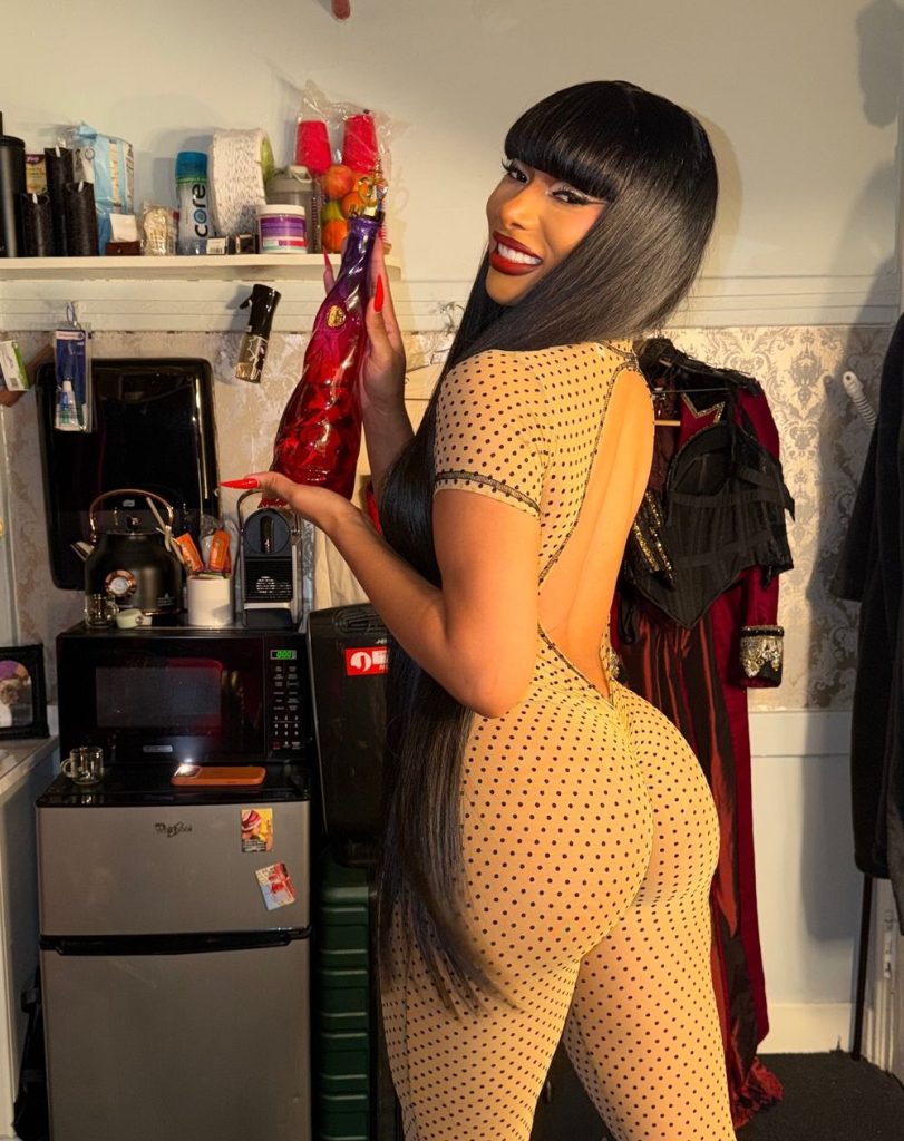 Backside view of Megan Thee Stallion smiling while wearing a tight catsuit inside a dressing room.