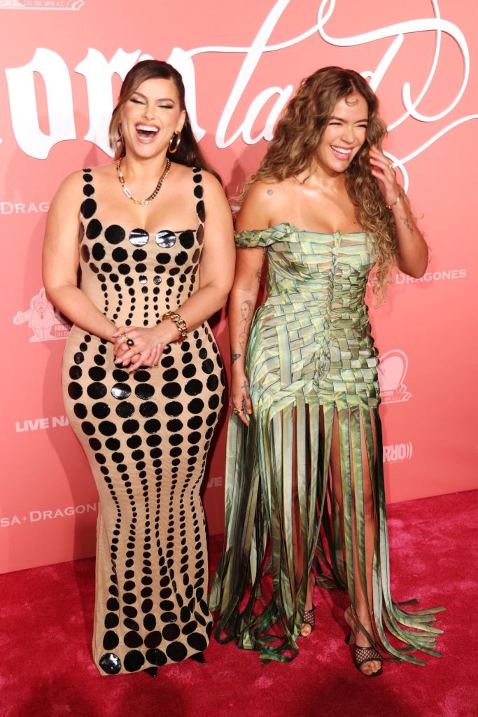 Two women in stylish dresses laughing on the red carpet.