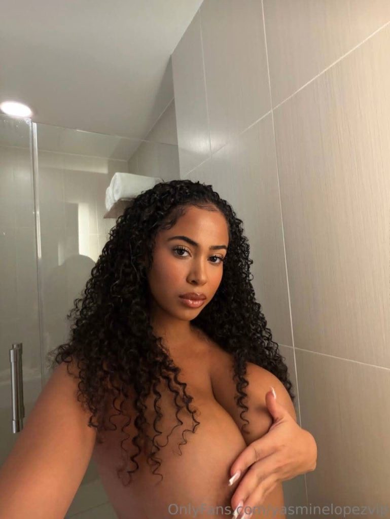 A topless woman covers her breasts with her hand when taking a selfie in a bathroom mirror.