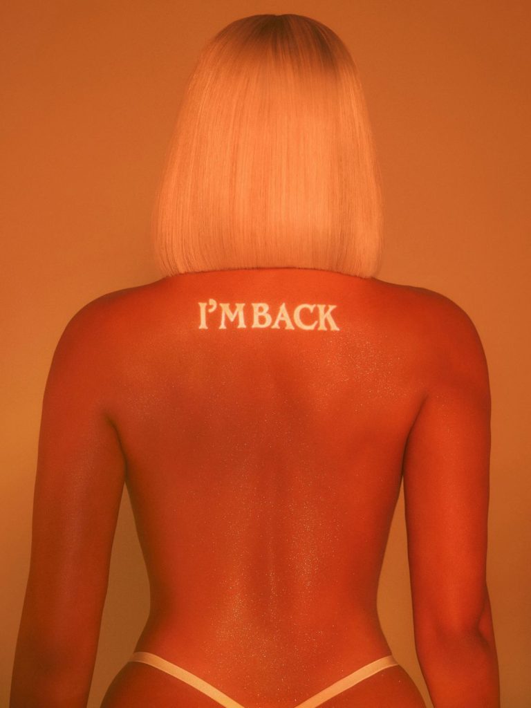 A woman with straight blonde hair is seen from behind, wearing white bottoms. IM BACK is written in white letters on their upper back. The image has a warm, orange tone.
