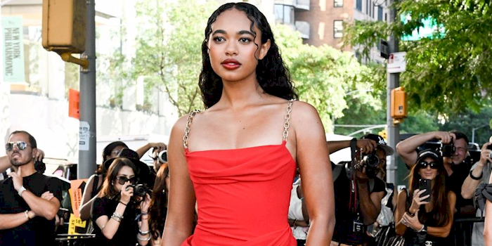 Close up of a woman in a red dress outdoors, surrounded by people taking photos.