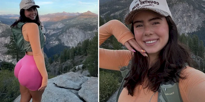 A female hiker wearing a baseball cap and orange long-sleeved shirt poses in front of a mountain landscape.