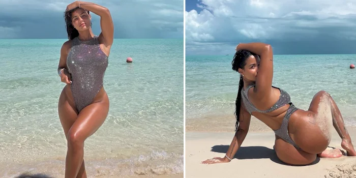 A woman posing on a beach in a high-cut, shimmering silver metallic one-piece swimsuit, shown standing in shallow water and sitting on the sand.