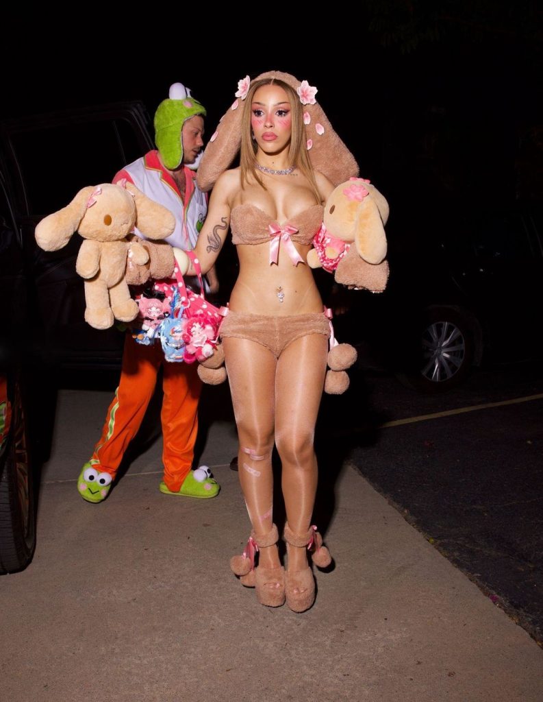 A woman in a fuzzy bunny-eared costume with plush toys, walking behind a person in a frog-themed tracksuit.