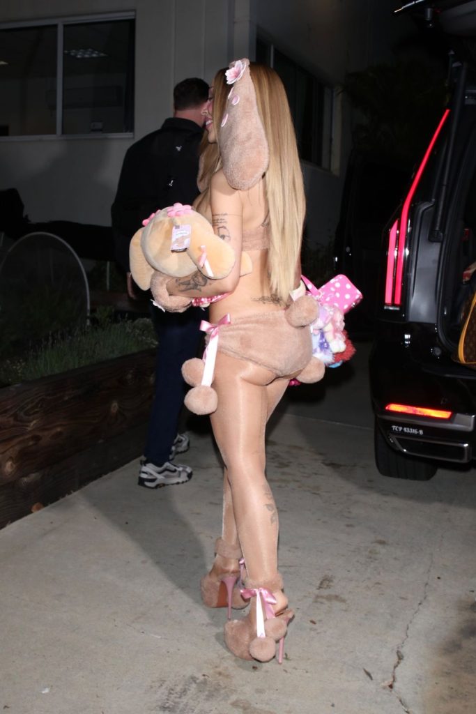 A person dressed in a fuzzy tan bunny costume with ears and a tail, wearing high-heeled platform shoes and carrying a stuffed animal.