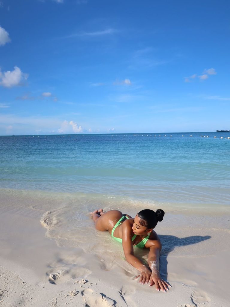 A woman in a neon green bikini lying in the shallow surf of a tropical beach.